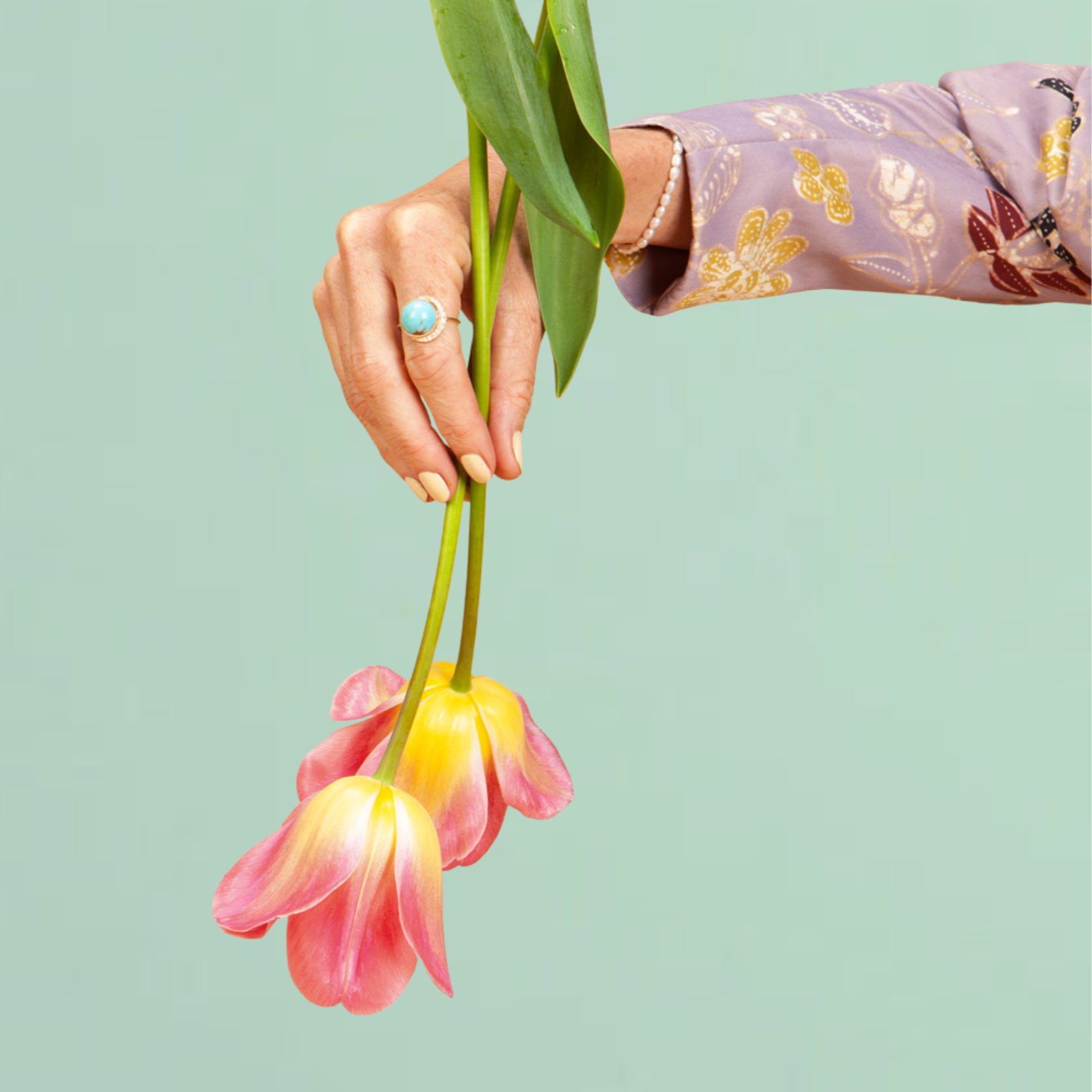 Hand holding pink and yellow flowers against a light green background