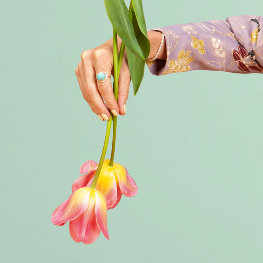 Hand holding pink and yellow flowers against a light green background
